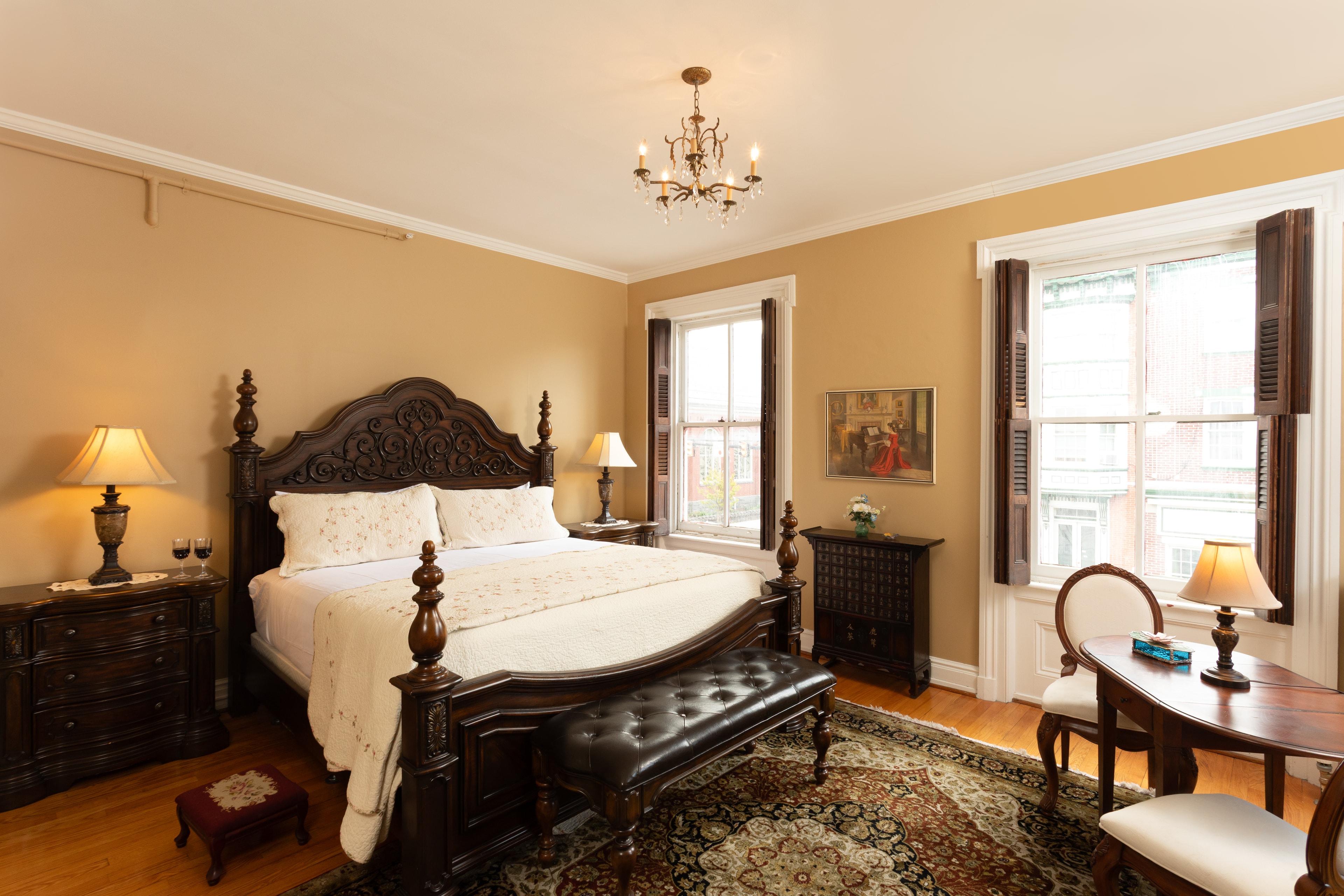A beautifully decorated bedroom featuring an ornate wooden bed, charming lamps, and large windows.