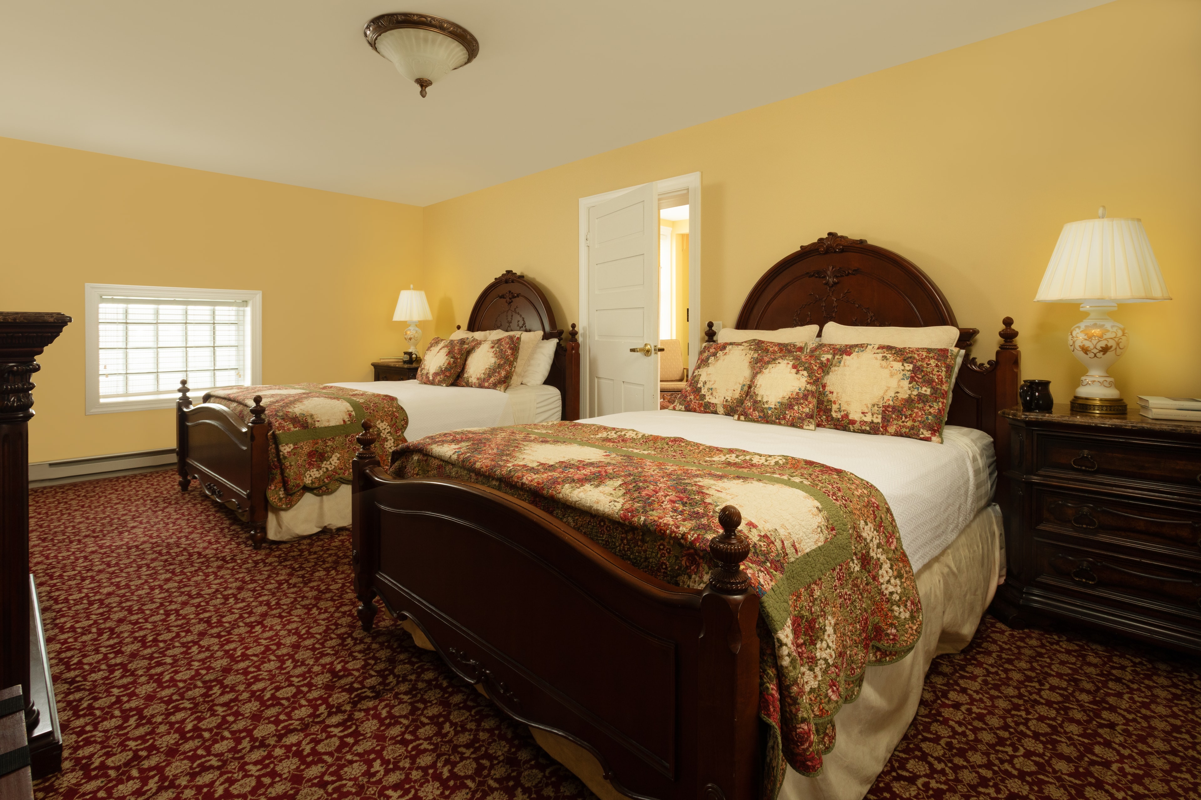 A cozy guest room featuring two wooden beds with ornate headboards, decorative quilts, and warm lighting.