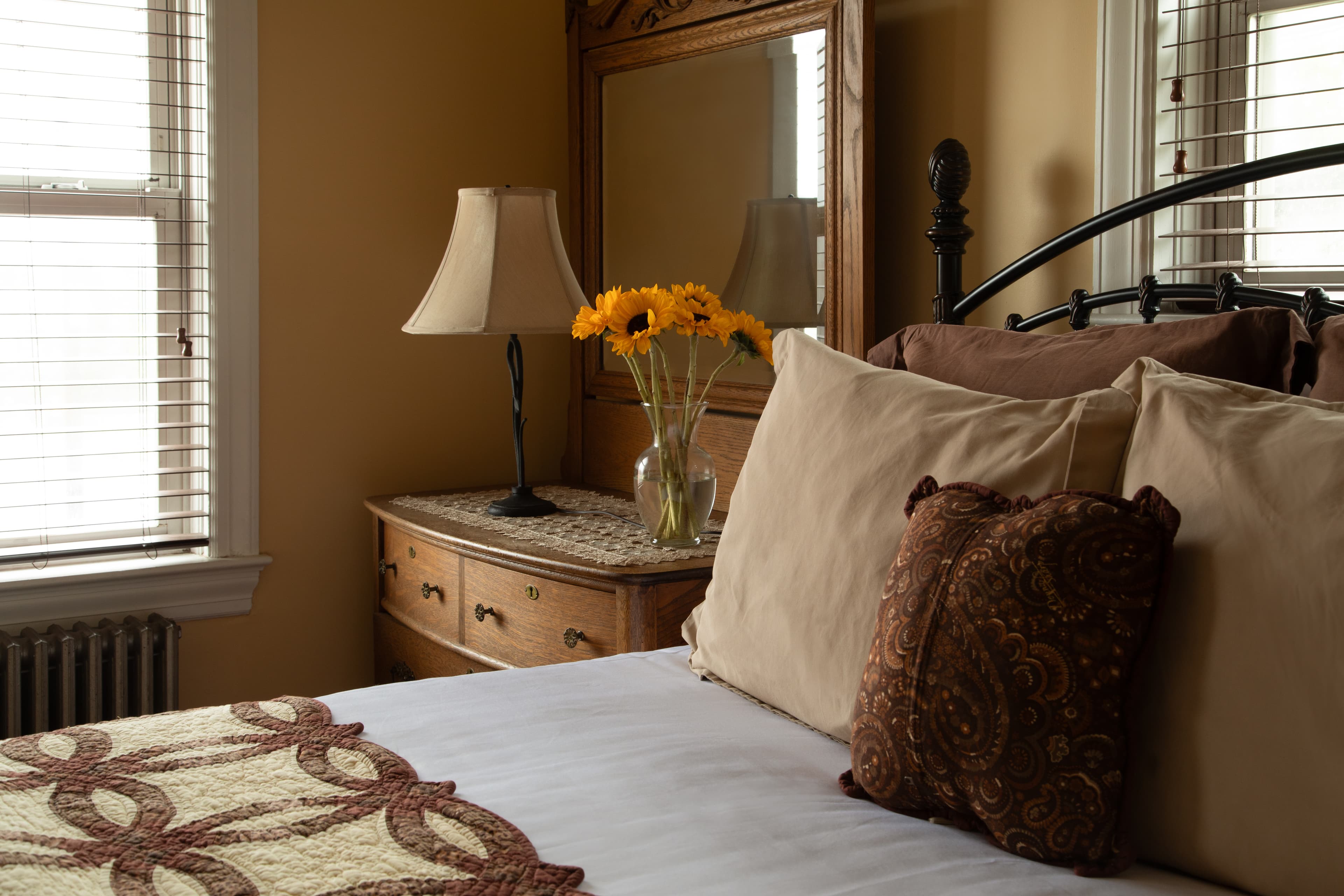 Cozy bedroom featuring a bed with decorative pillows, a wooden dresser, and a vase of sunflowers on a nightstand.