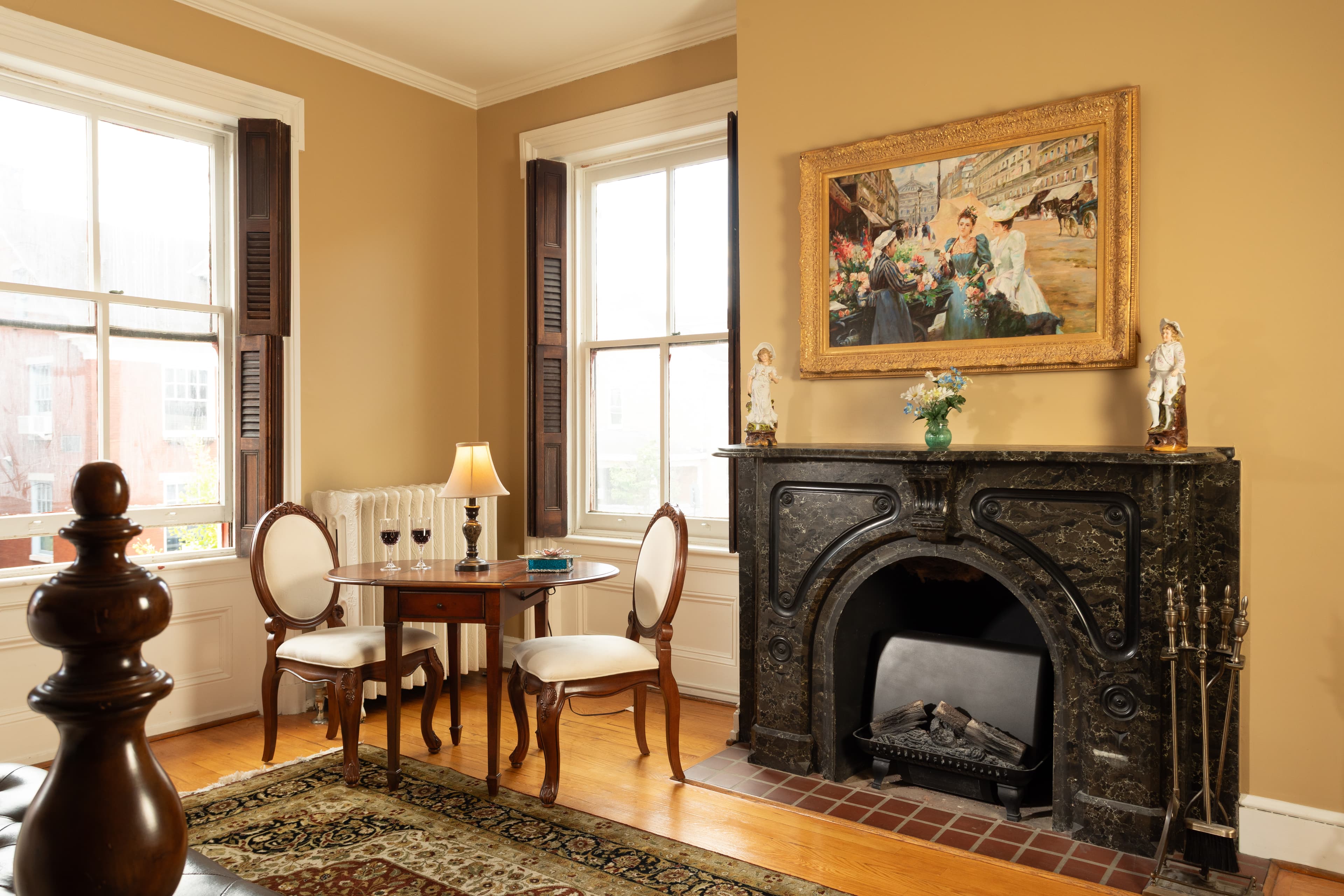 A cozy corner of a room featuring a small table with two chairs, a lamp, and a decorative fireplace adorned with a painting.