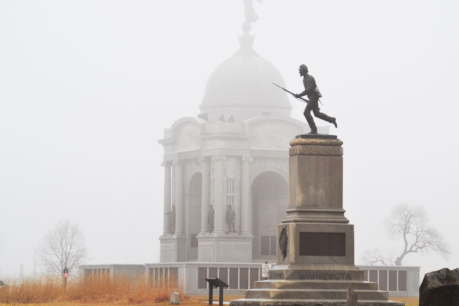 A soldier statue stands in front of a grand memorial shrouded in fog.