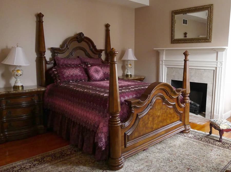 A luxurious bedroom featuring a wooden four-poster bed with rich burgundy bedding, flanked by bedside lamps and a decorative mirror.