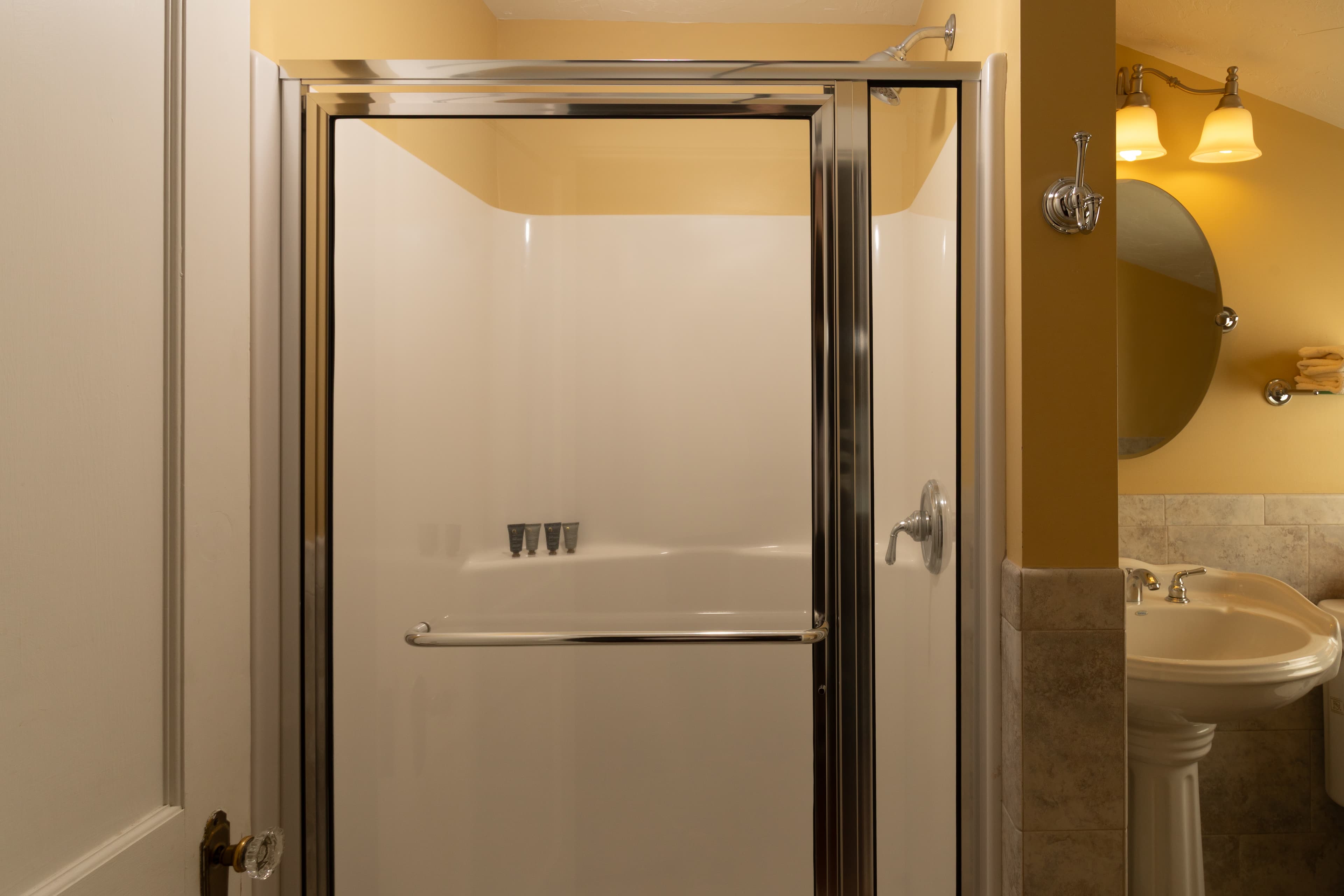 A small bathroom featuring a glass shower, a sink with a mirror, and a toilet against yellow walls.