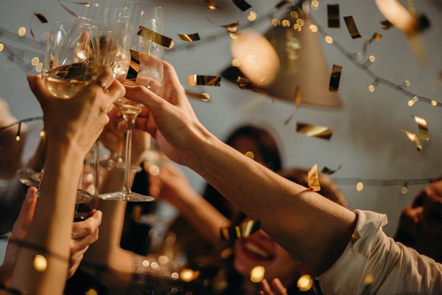 A group of hands clink glasses in celebration amidst falling confetti.