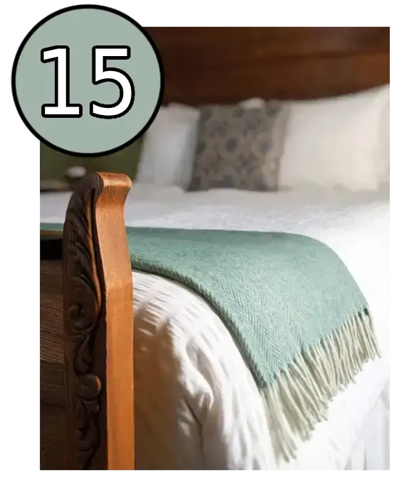 Close-up of a carved wooden bed frame and a light green blanket draped over a white bed.