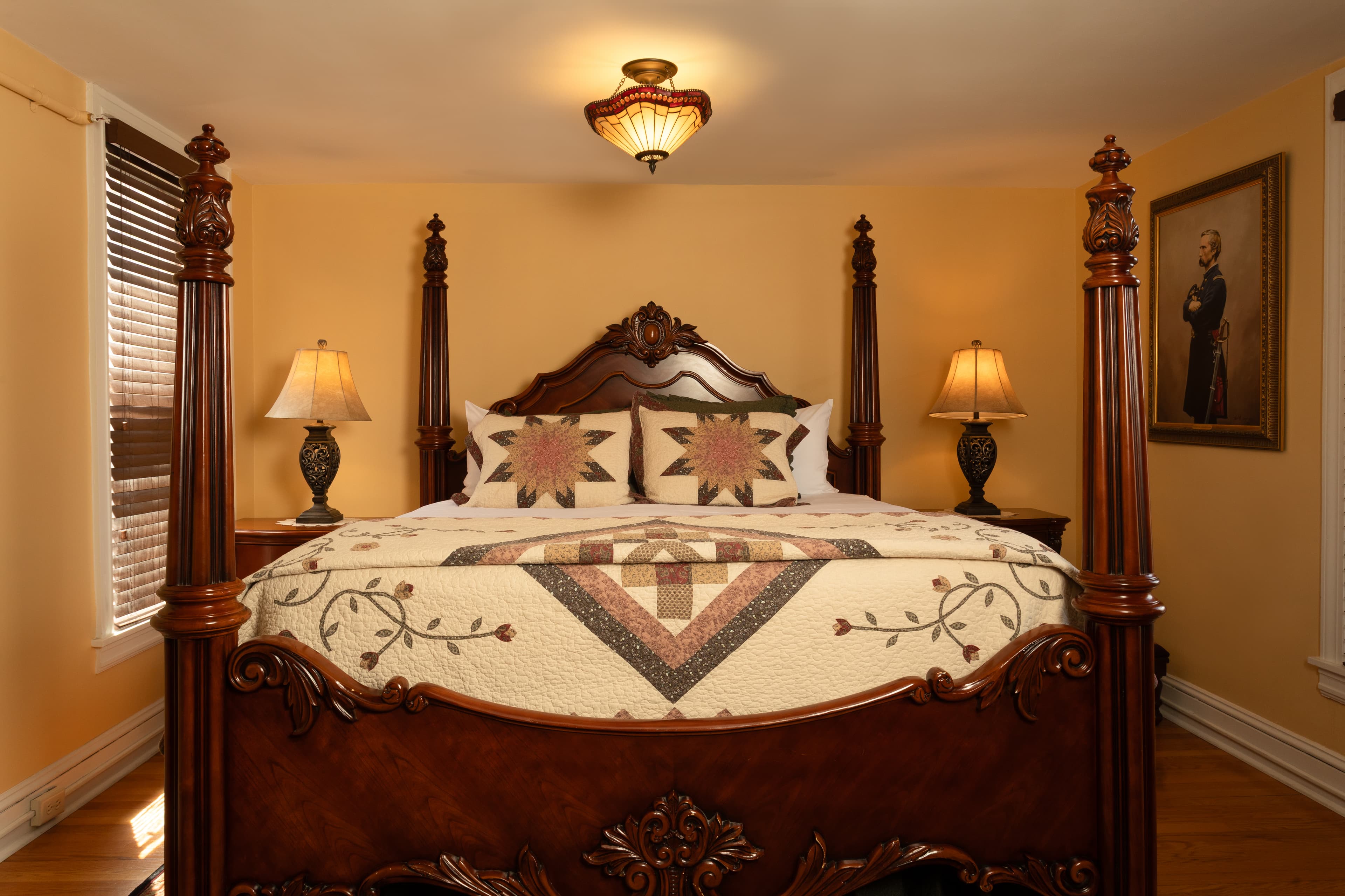 A cozy, warmly-lit bedroom featuring a four-poster bed with decorative bedding and two bedside lamps.