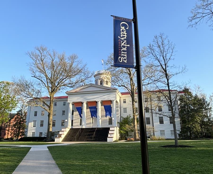 Gettysburg College building with a prominent flag and clear blue sky.