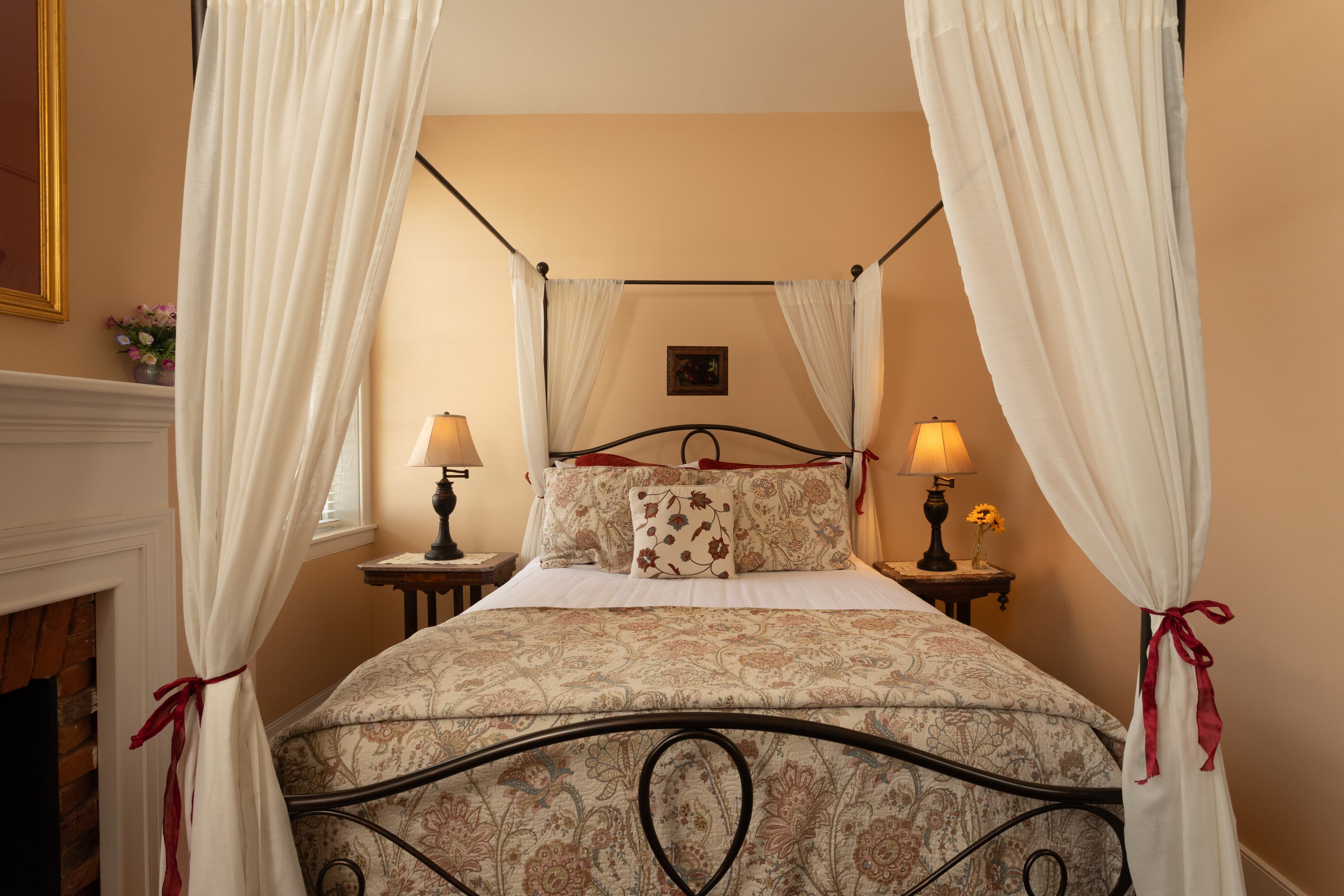 A cozy bedroom featuring a four-poster bed with sheer curtains and bedside lamps.