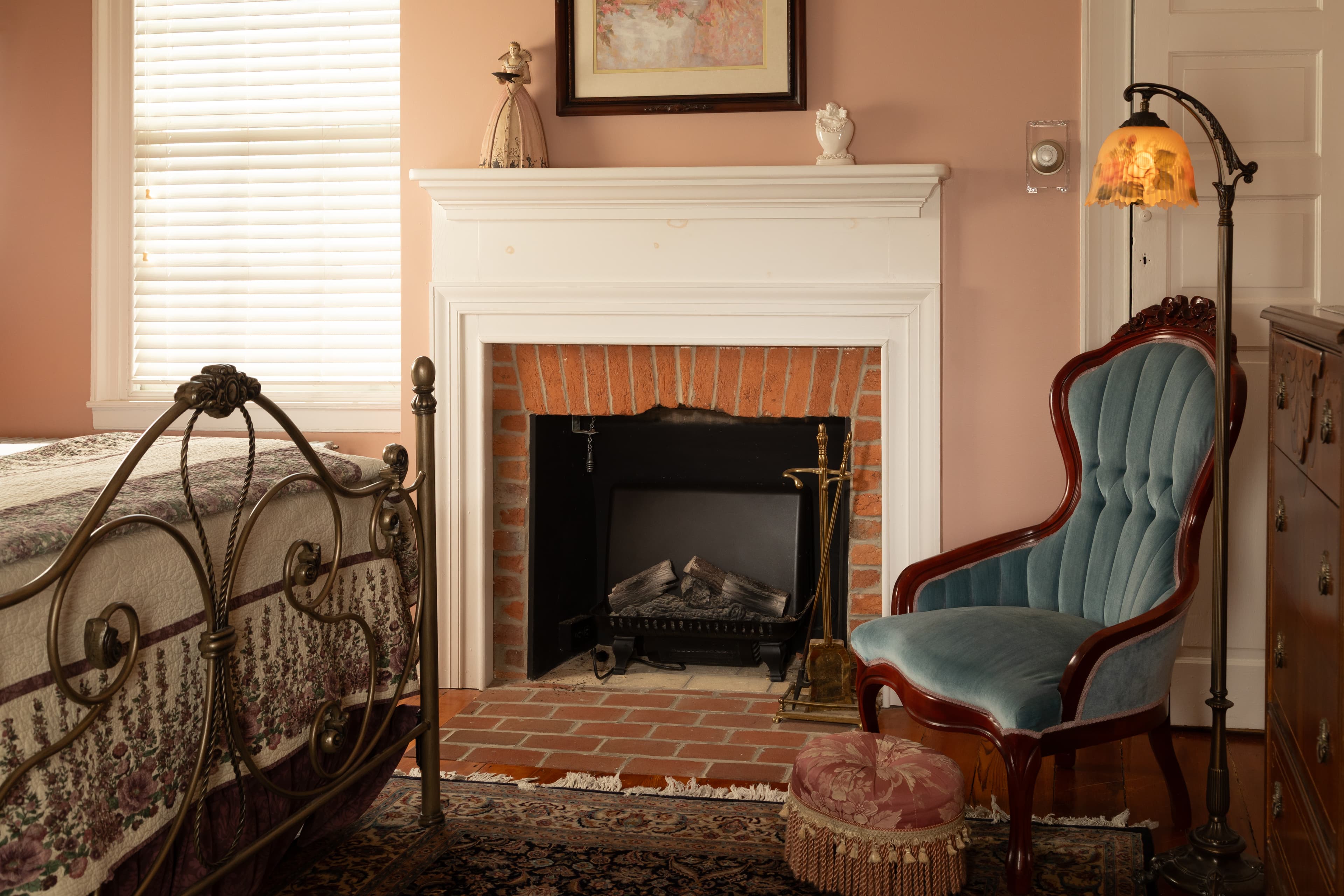 A cozy bedroom featuring a metal bed, a blue upholstered chair, and a decorative brick fireplace.
