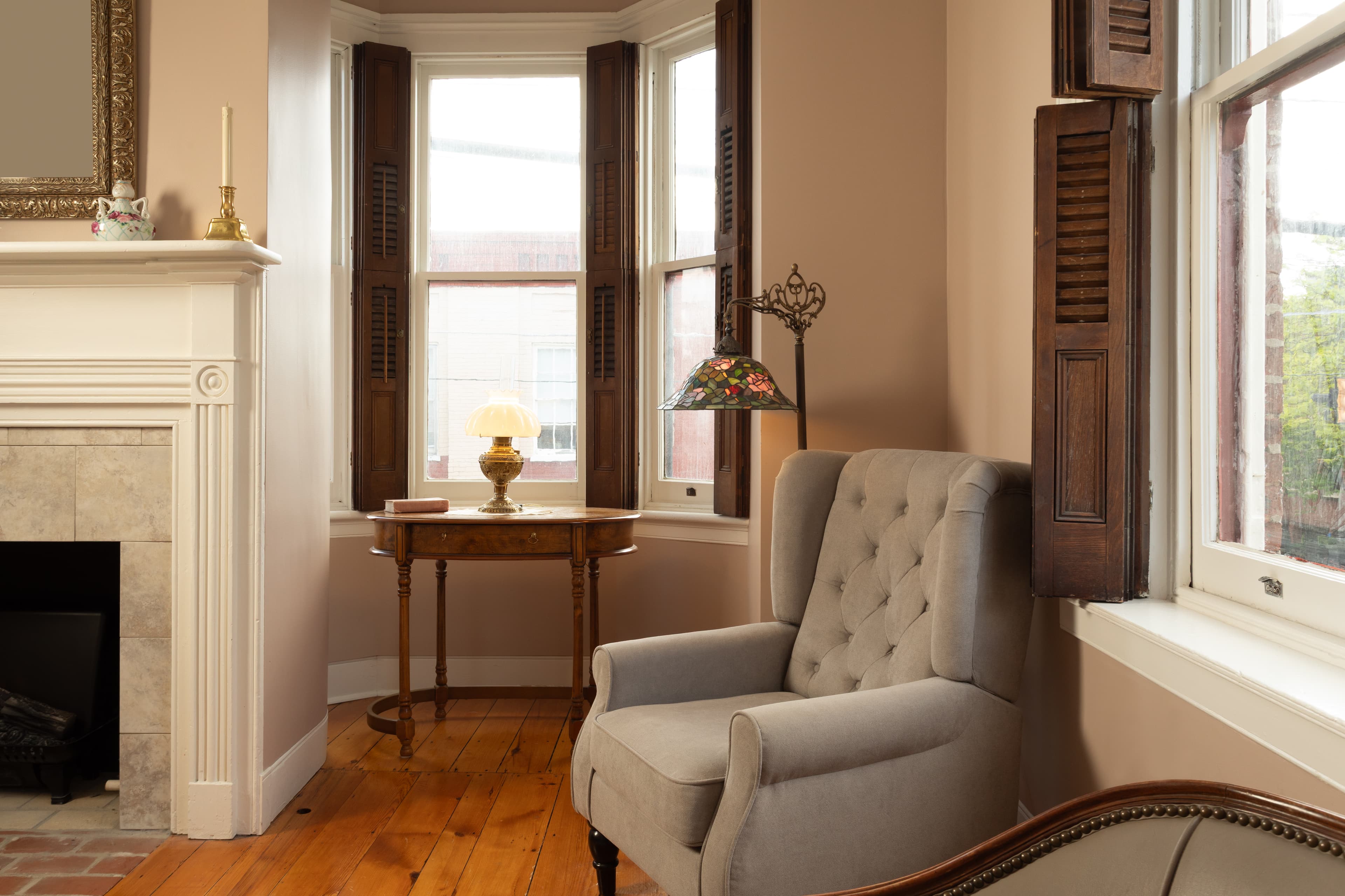 Cozy living room corner featuring a tufted gray armchair next to a small table and a decorative lamp by a window.