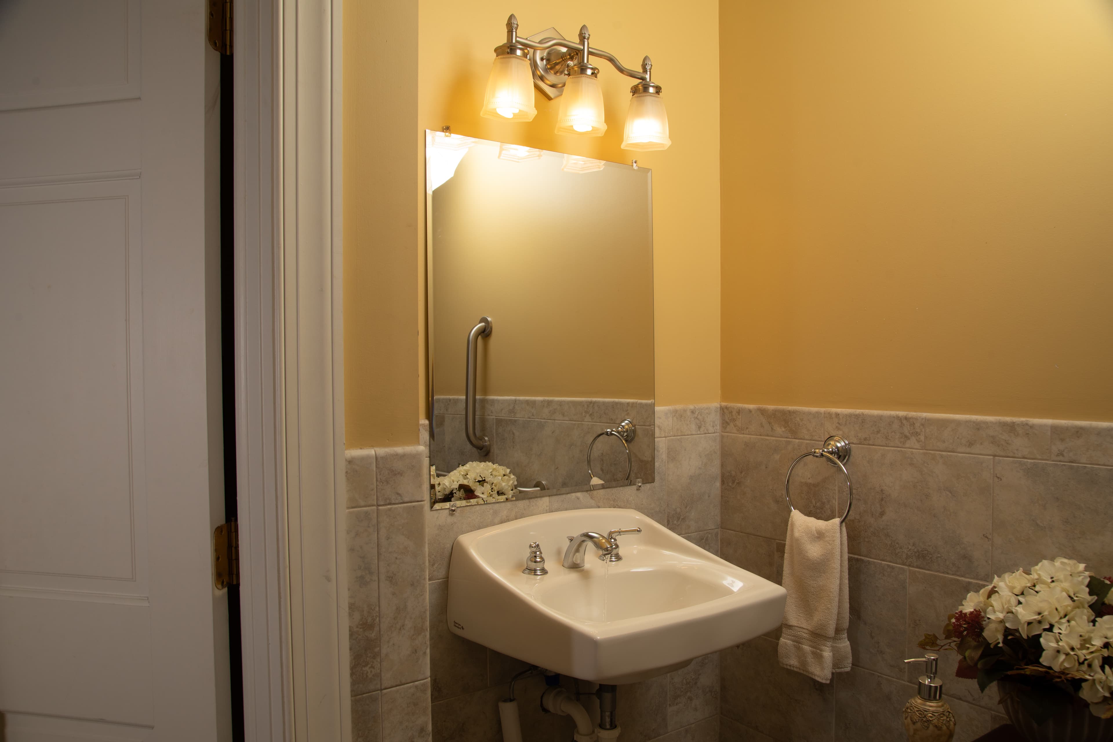 A small bathroom features a wall-mounted sink, mirror, and light fixtures against a yellow wall.