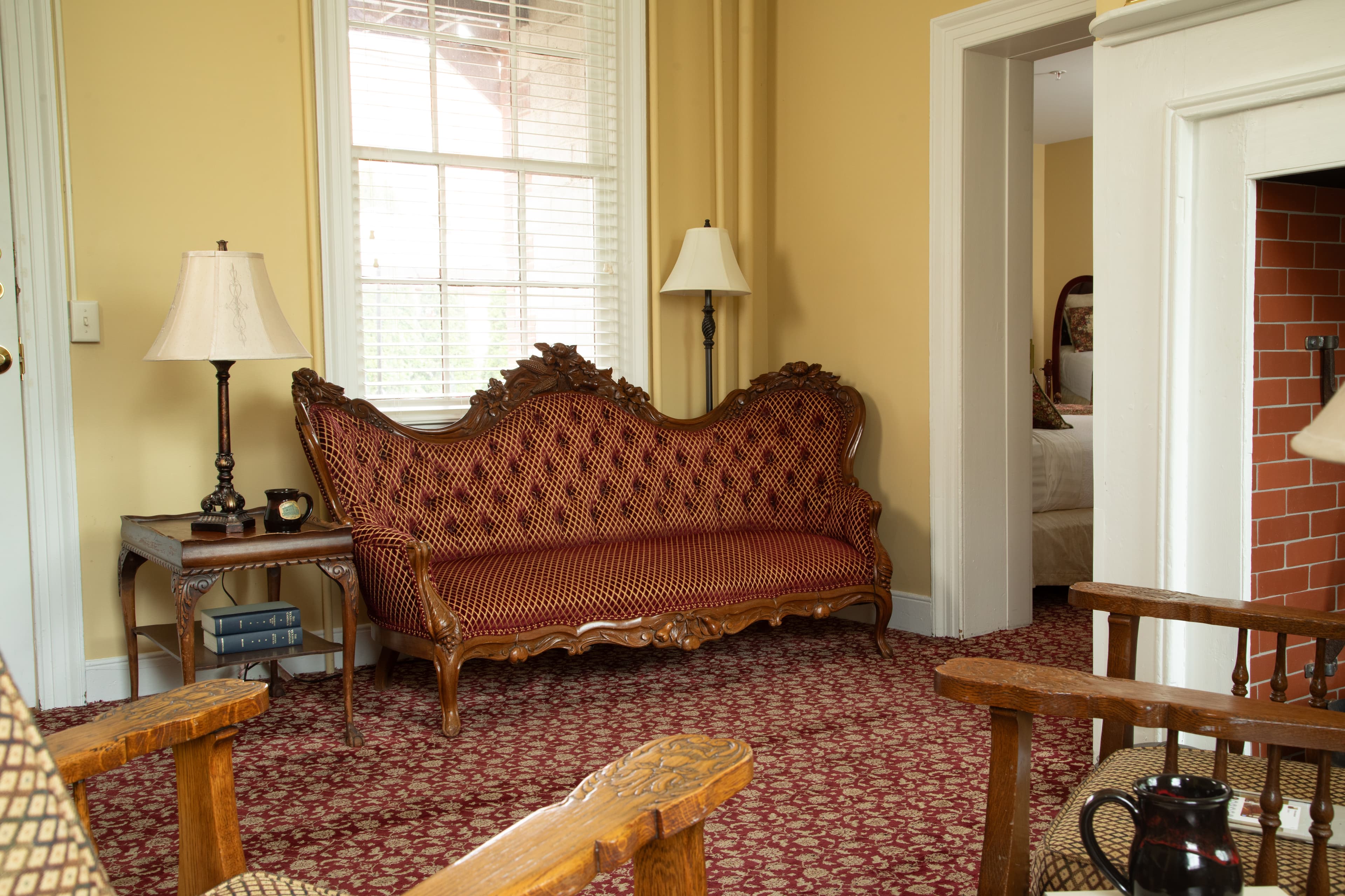 A vintage red patterned sofa with wooden legs sits in a cozy room featuring two lamps and a doorway leading to another space.