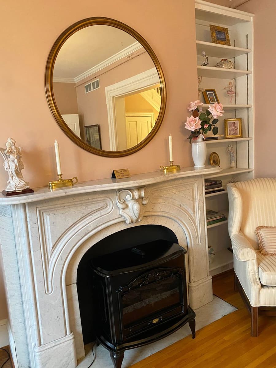 A marble fireplace adorned with a round mirror, candles, and decorative items in a cozy living room.