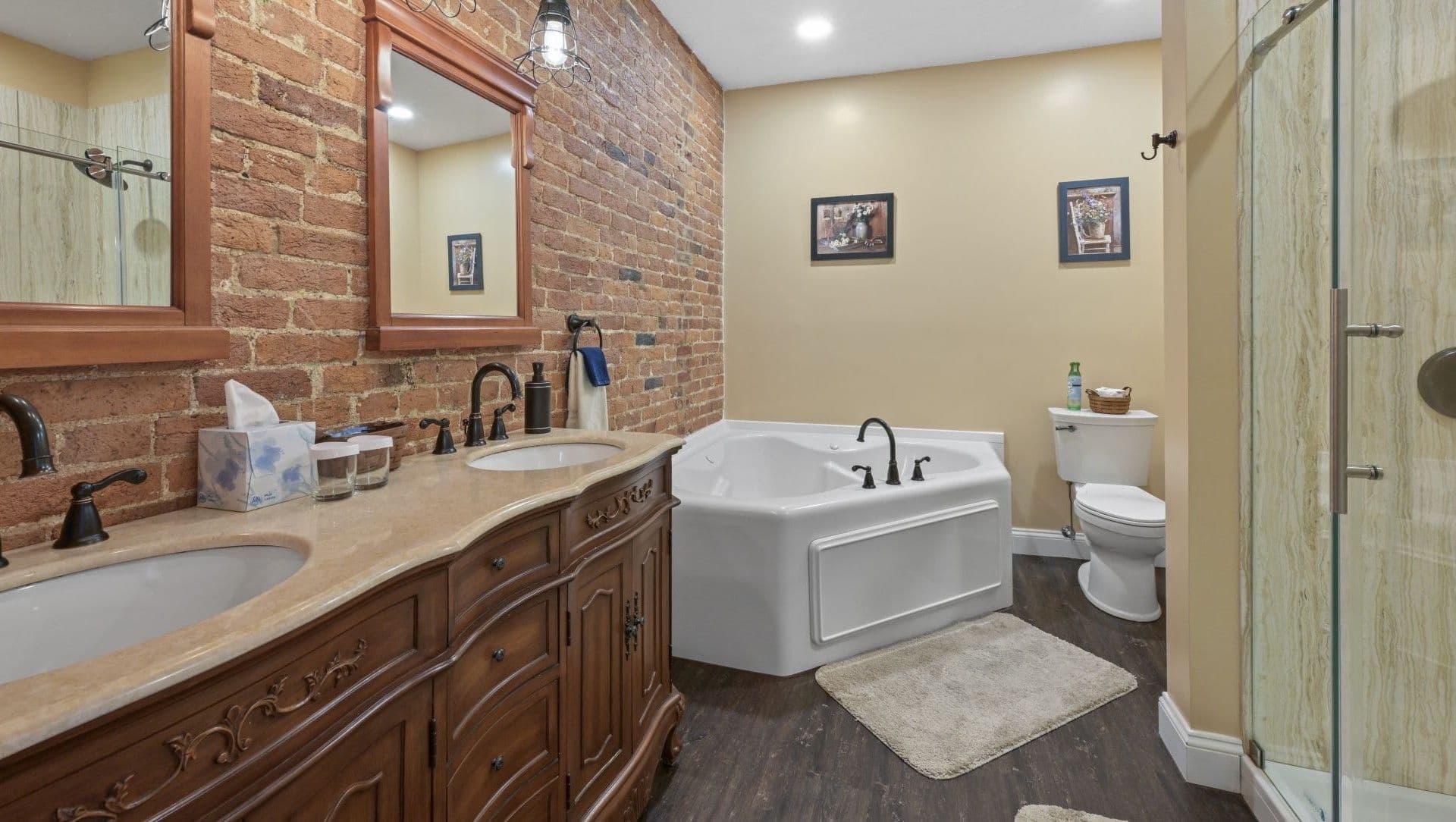 Modern bathroom featuring a wooden vanity, a jacuzzi tub, and a separate shower area with exposed brick walls.
