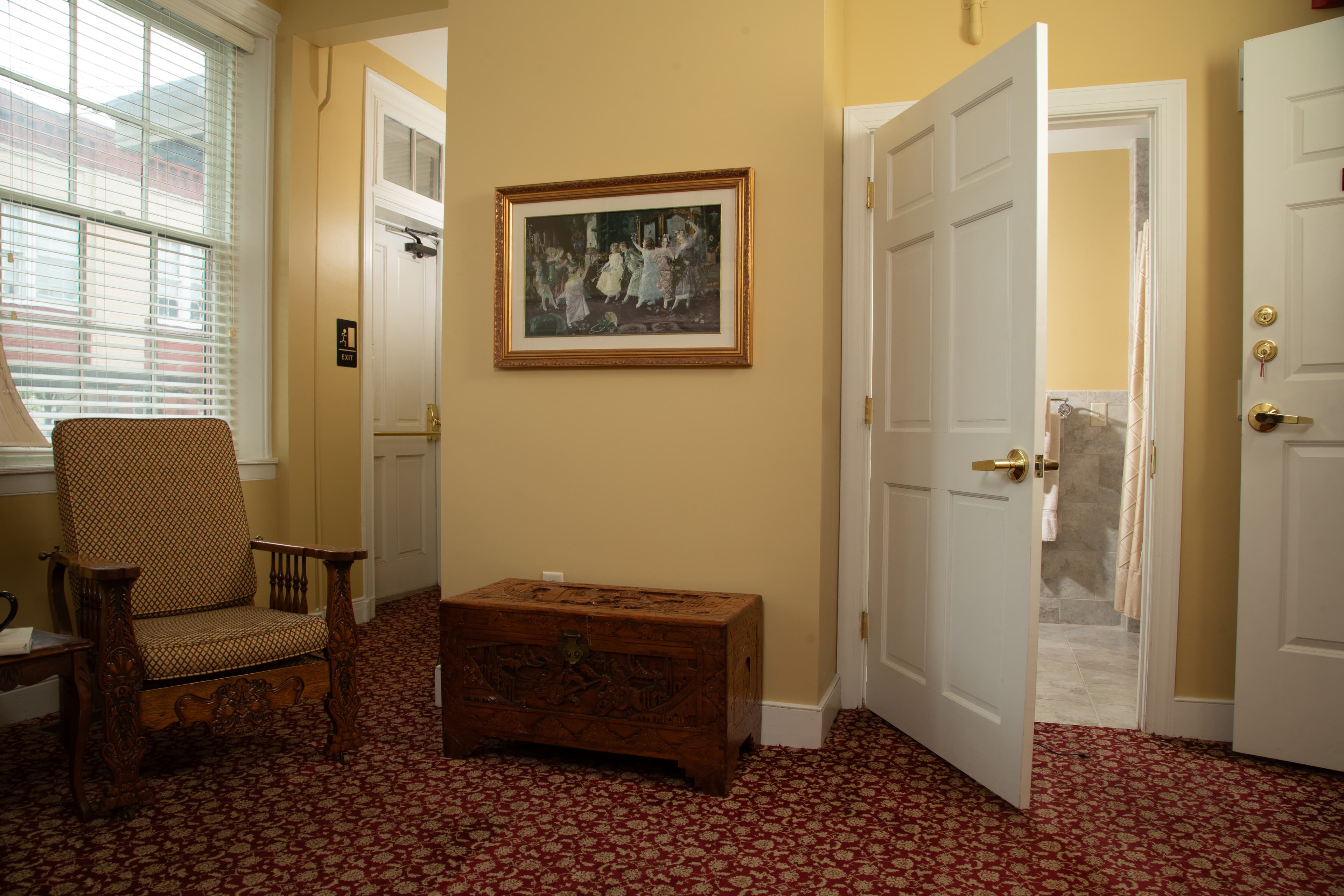 A cozy hallway with a wooden chair, a decorative chest, and two open doors showing a bathroom.