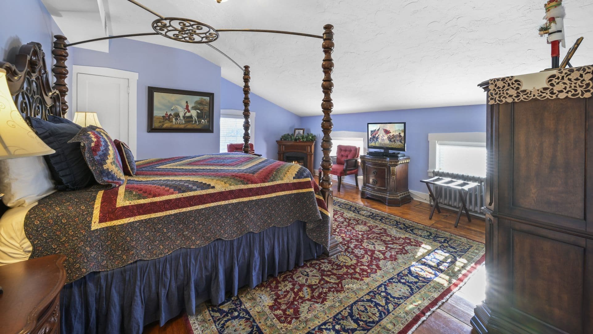 A cozy bedroom featuring a colorful quilted bed, decorative wooden furniture, and a small seating area.