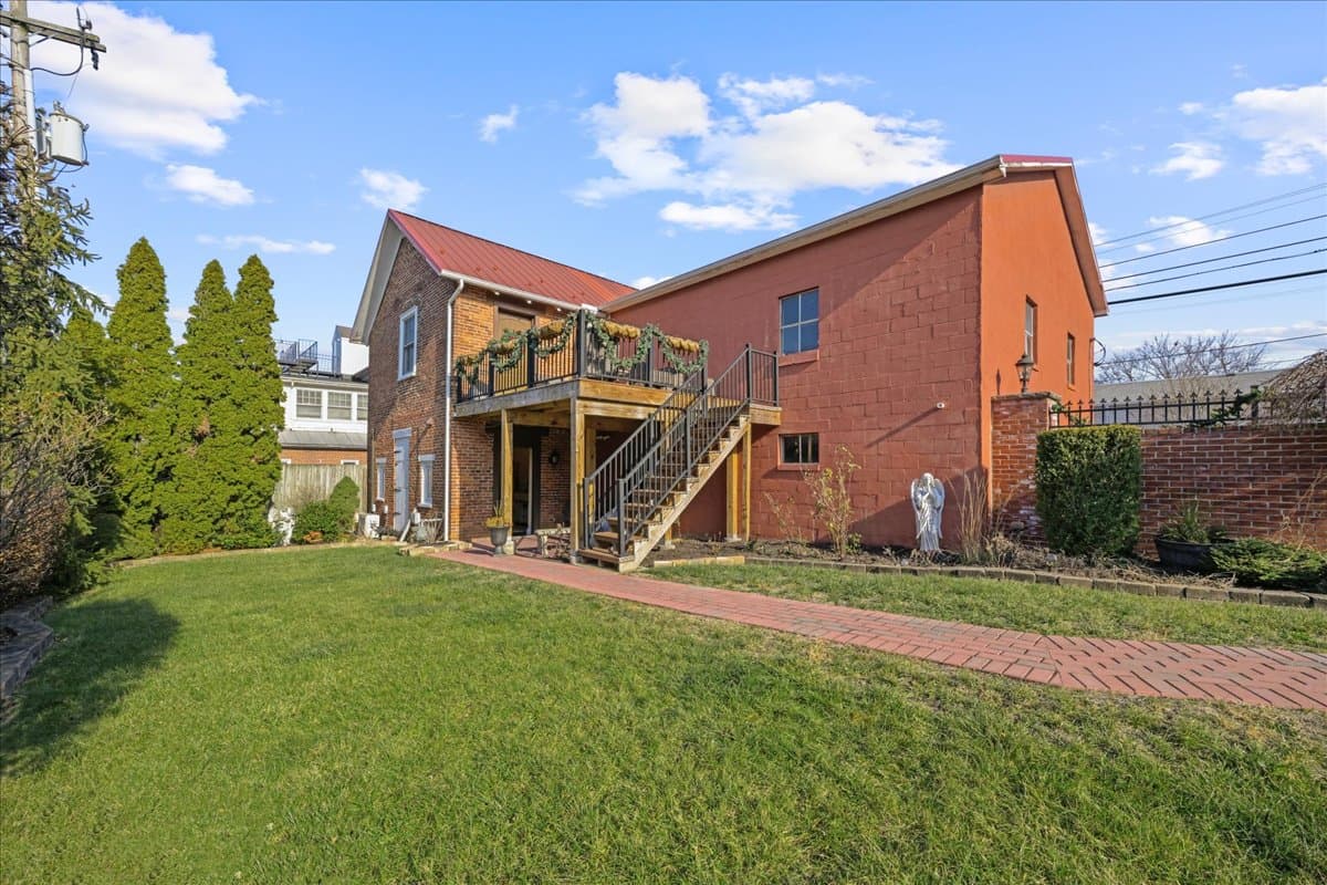 A two-story house with a red exterior, a wooden deck, and a landscaped lawn.