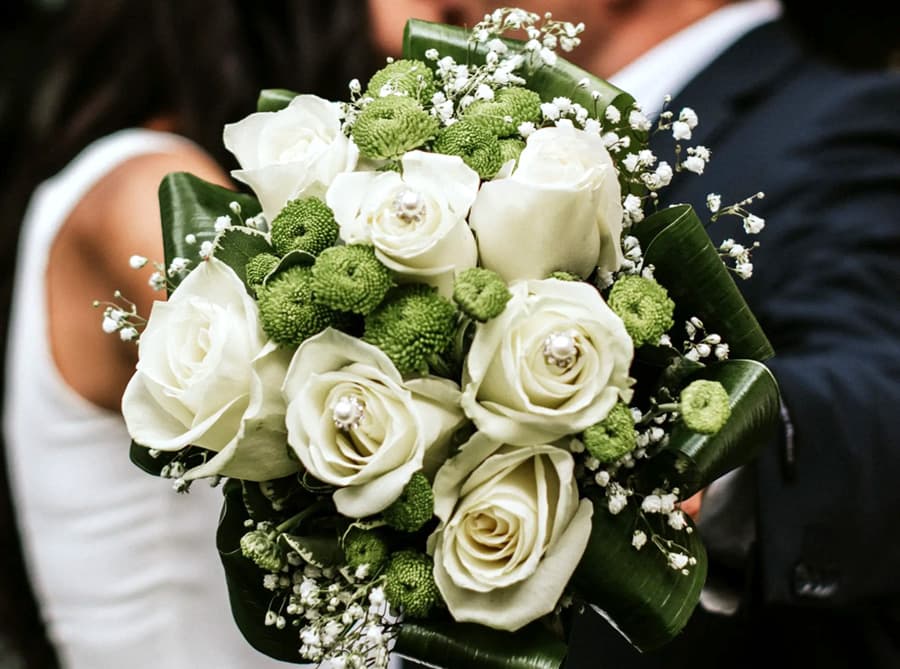 A bouquet of white roses and green pom-pom flowers held by a person.