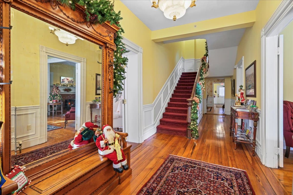A warmly decorated hallway features a large mirror, festive decor, and a staircase leading to the upper level.