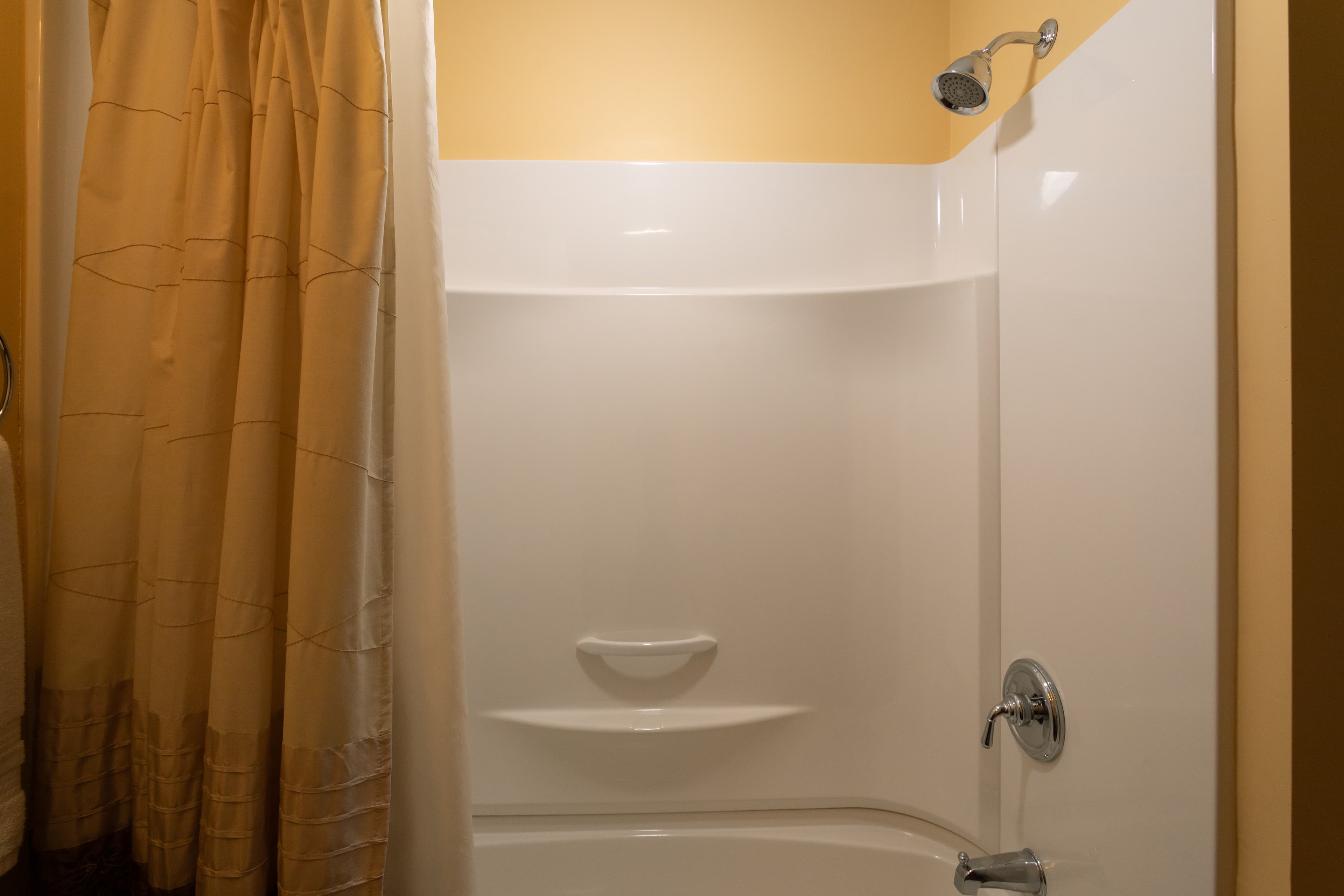 A clean, empty shower stall with a beige curtain and yellow walls.