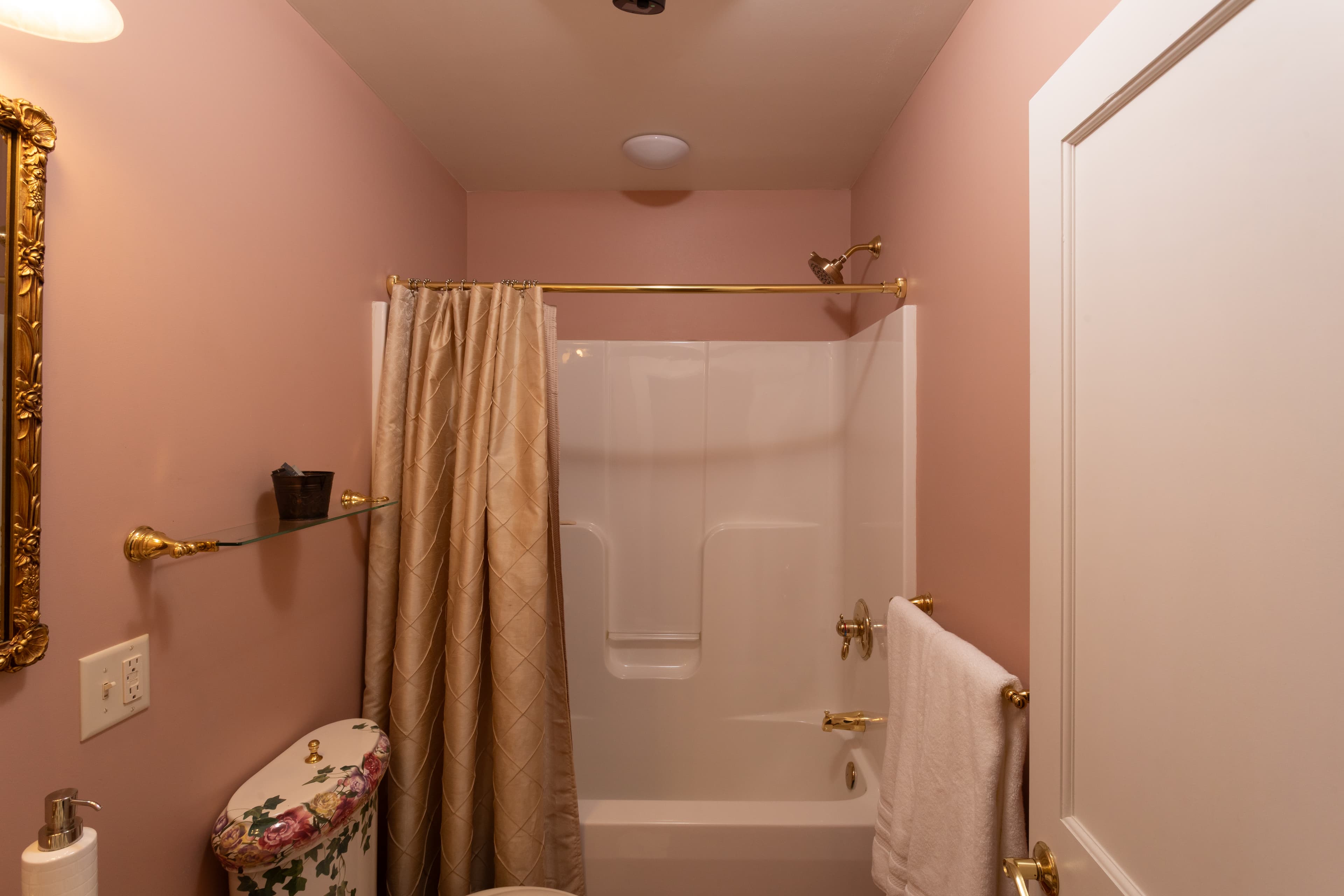 A pastel pink bathroom featuring a shower area, gold accents, and decorative elements.