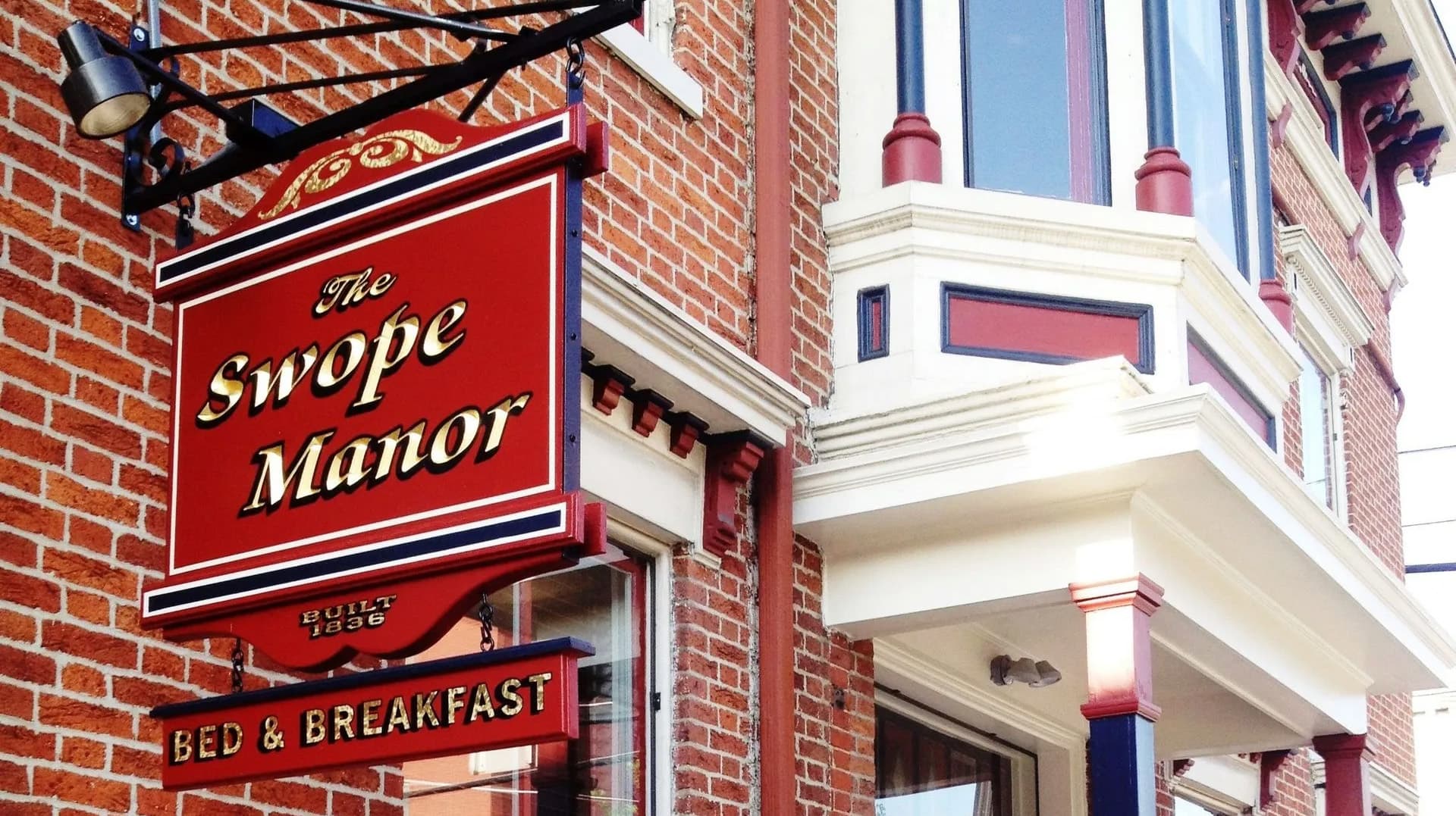 Signage for The Swope Manor Bed & Breakfast, featuring red and gold lettering against a brick wall.