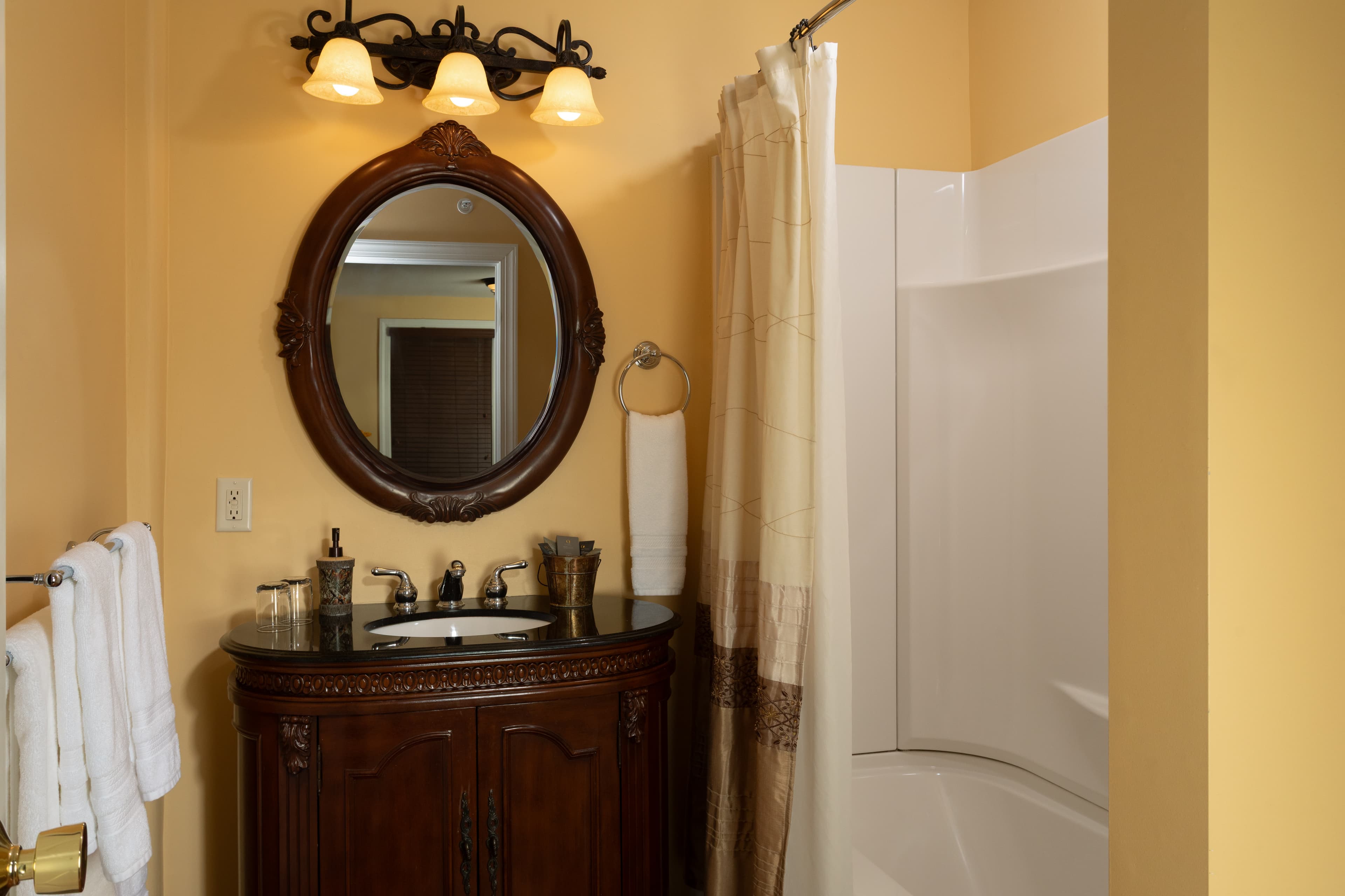A well-lit bathroom featuring a dark wooden vanity, round mirror, and a shower area with light-colored curtains.