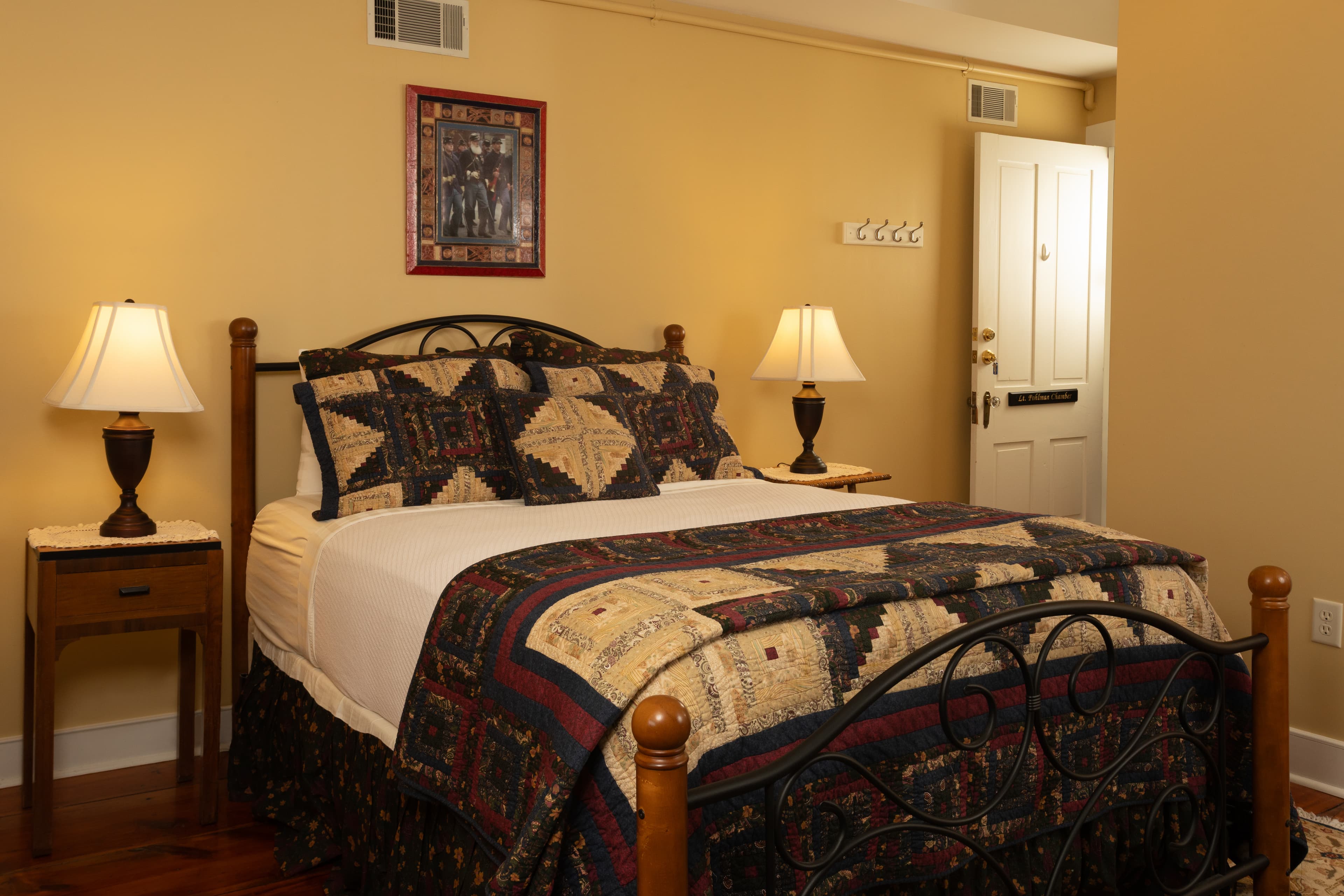 A cozy bedroom featuring a quilted bedspread, two bedside lamps, and a door leading outside.