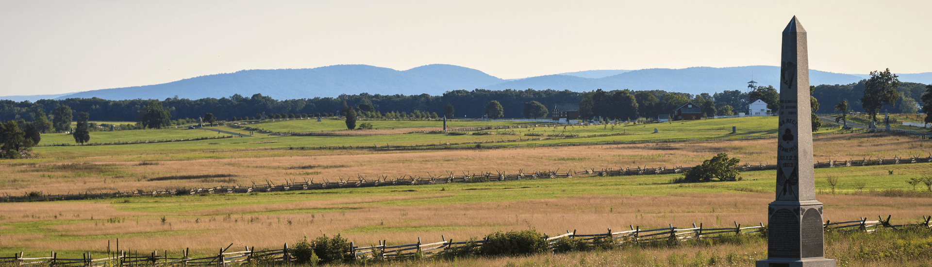 A vast grassy landscape with a monument in the foreground and mountains in the background.