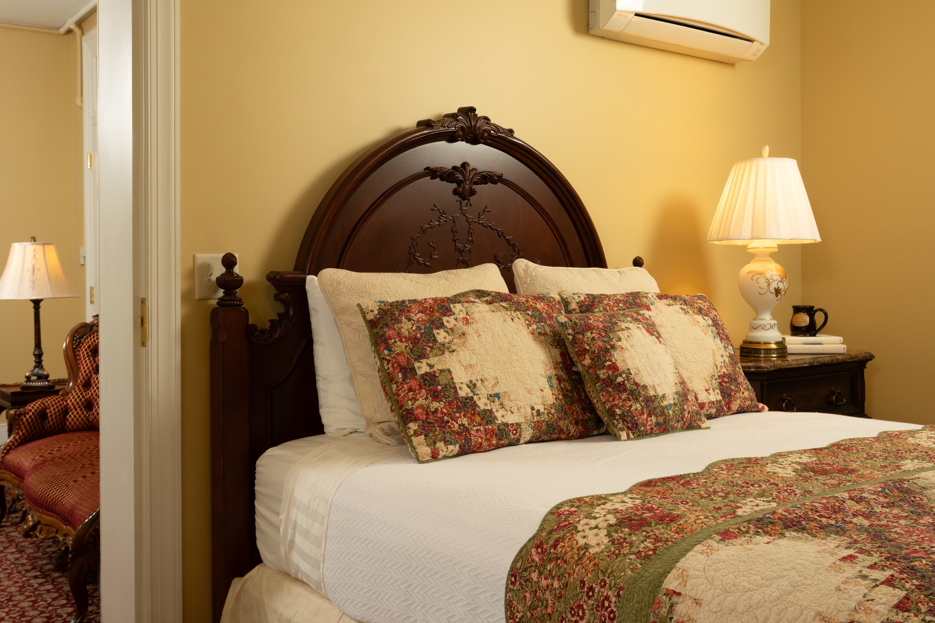 A cozy bedroom featuring a wooden bed with decorative pillows, a quilt, and softly lit lamps.