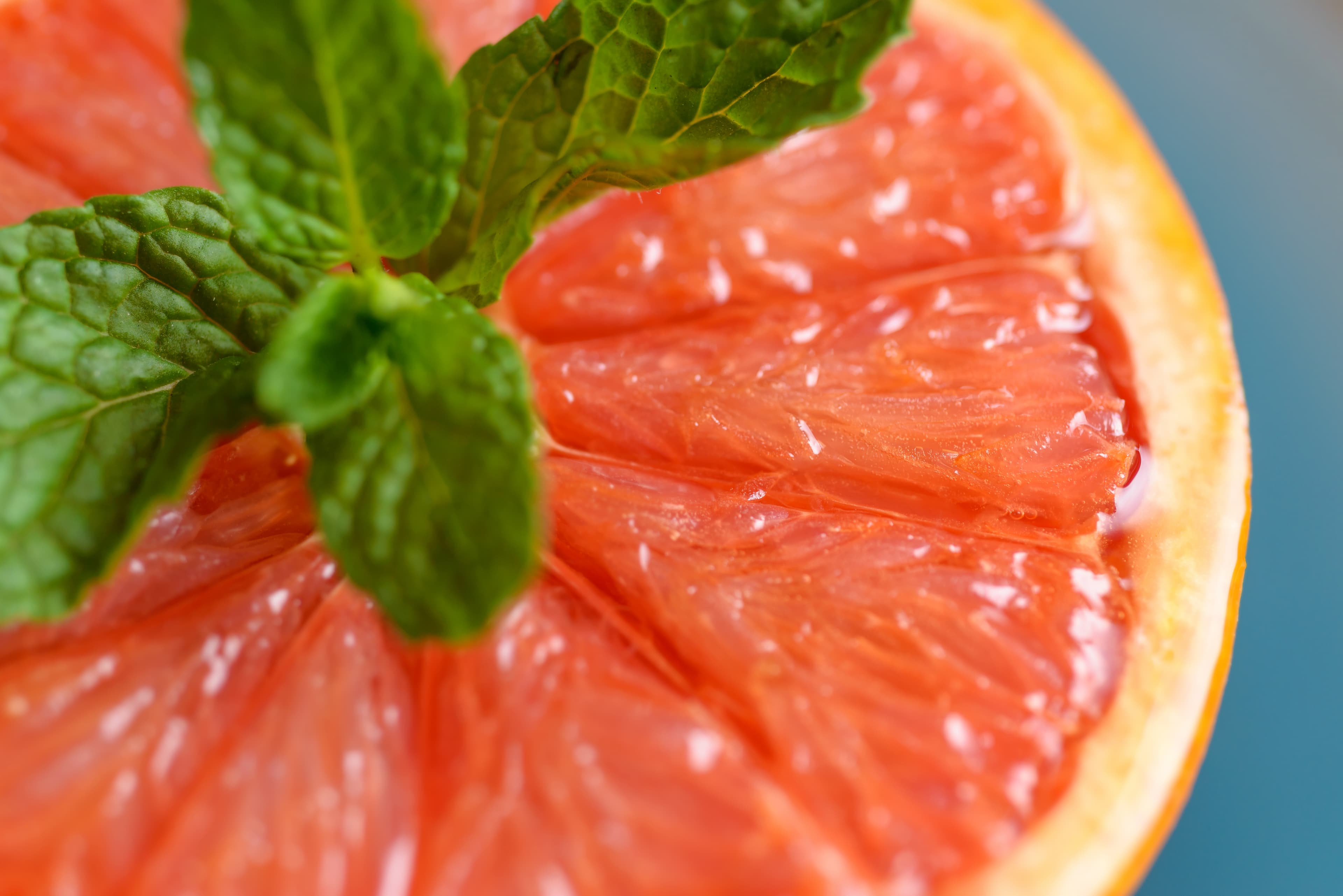 A close-up of a freshly cut pink grapefruit topped with a sprig of mint.