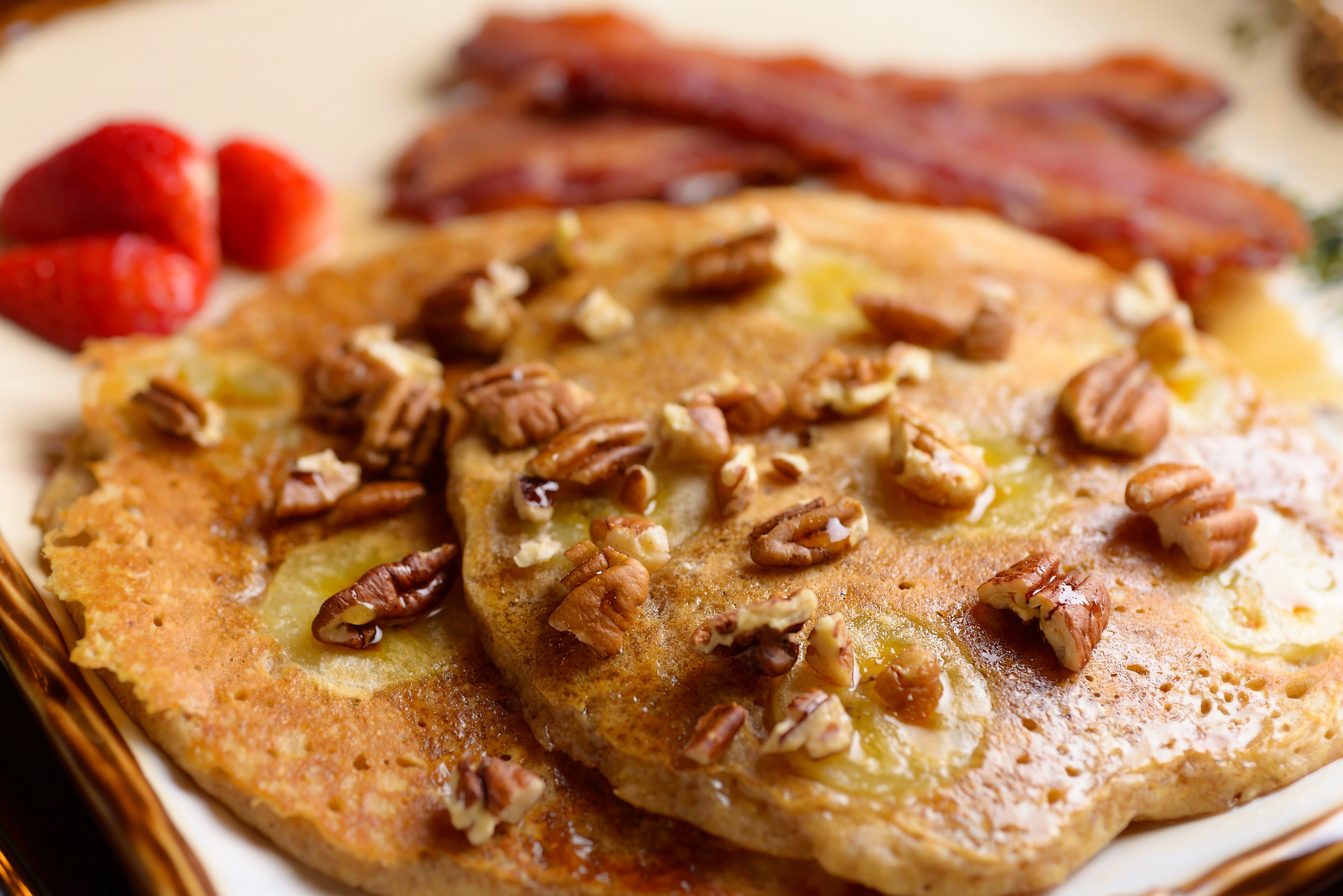 A plate featuring fluffy pancakes topped with pecans and accompanied by bacon and strawberries.