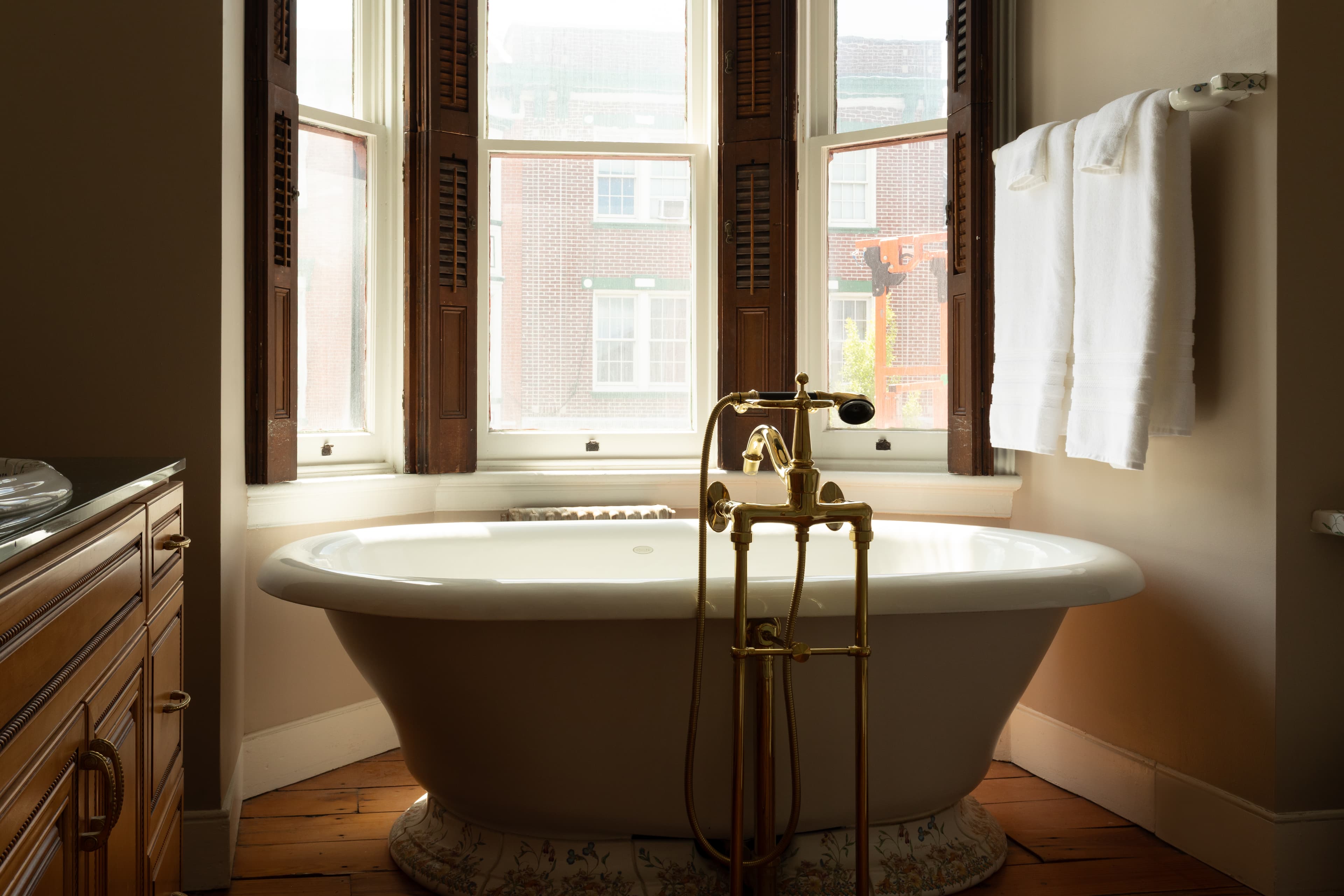 A vintage freestanding bathtub with a brass faucet sits next to a window, complementing a warm-toned bathroom.