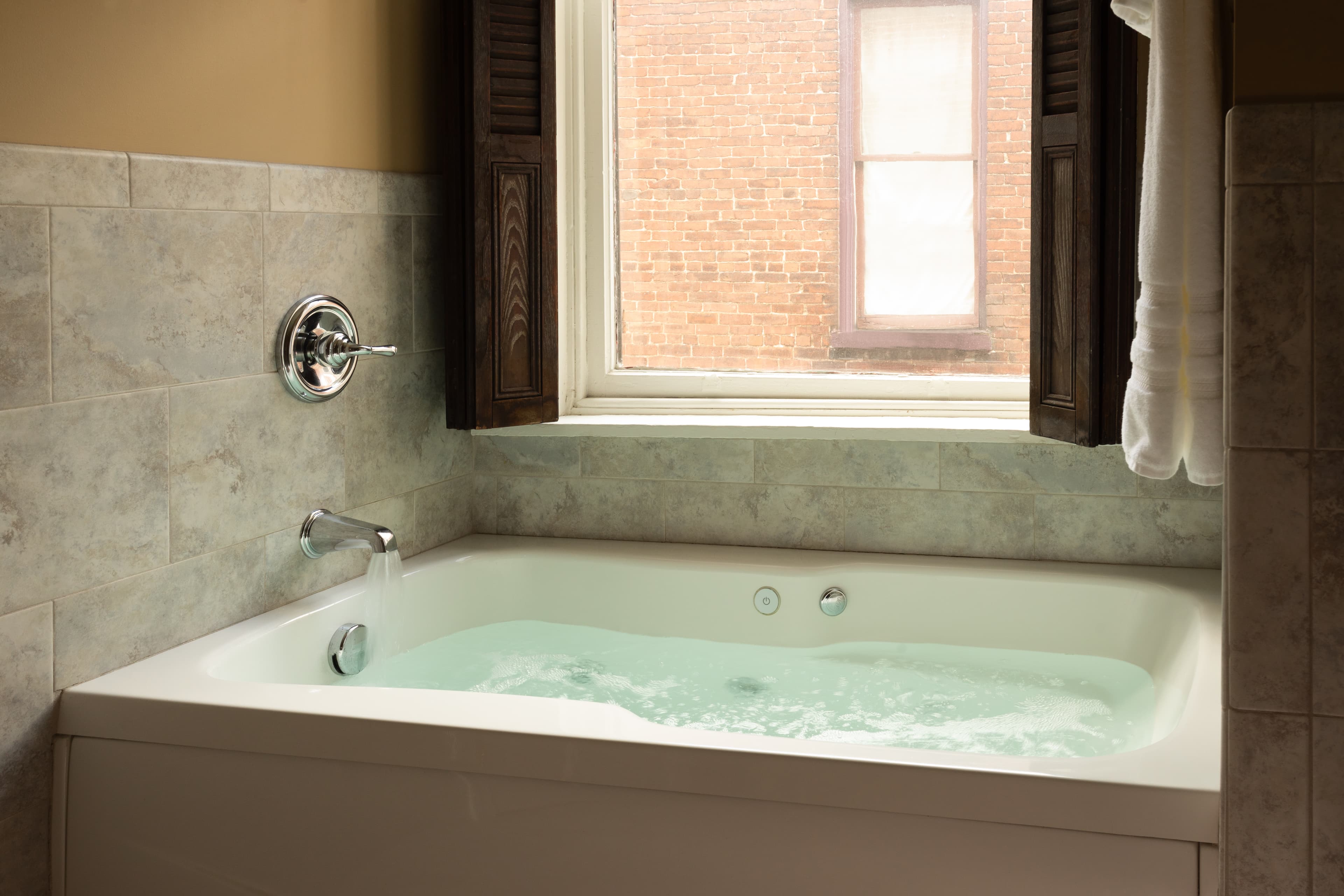 A modern bathtub with bubbling water near a window in a tiled bathroom.