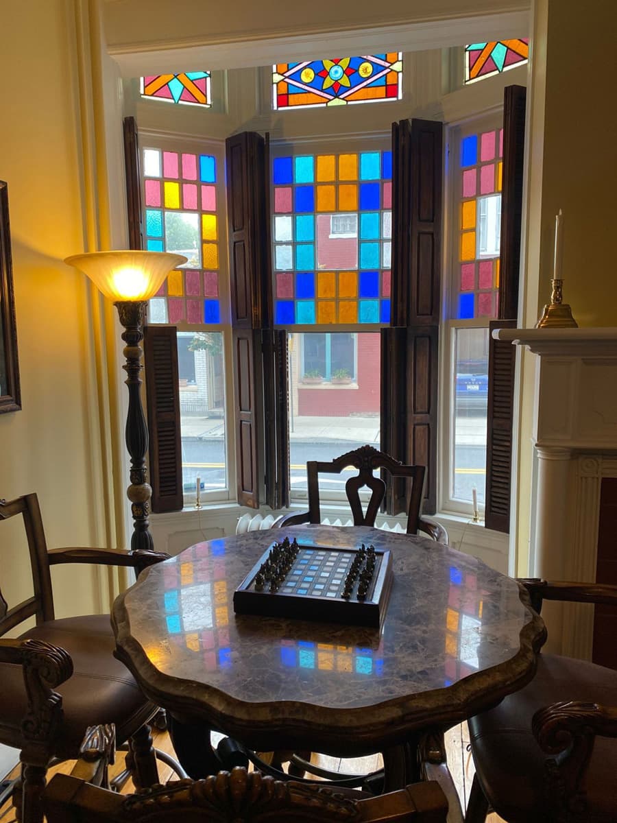 A cozy room featuring a marble-topped table with a chess set, illuminated by colorful stained glass windows.