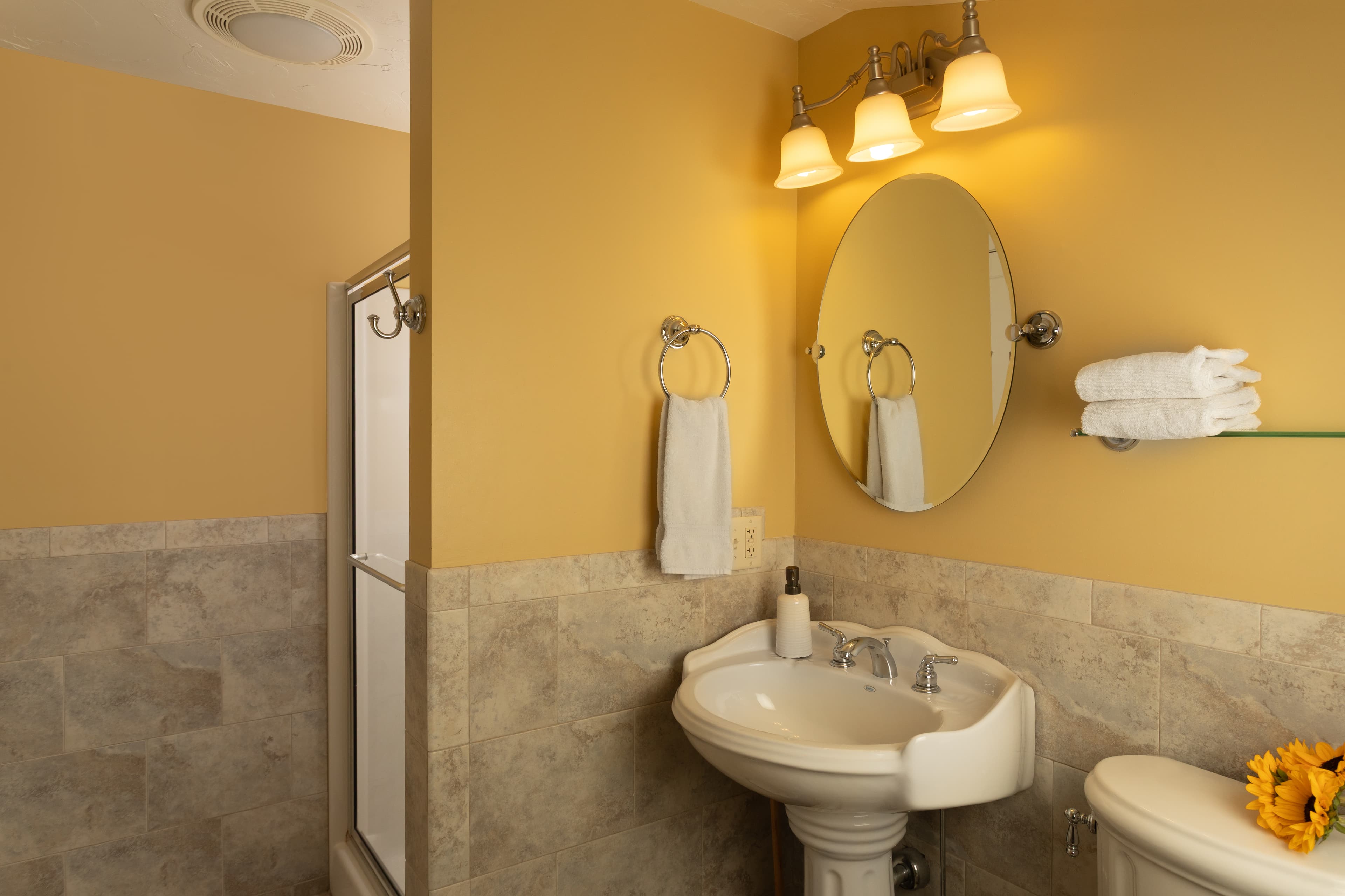 A cozy bathroom featuring a pedestal sink, mirror, and warm lighting.