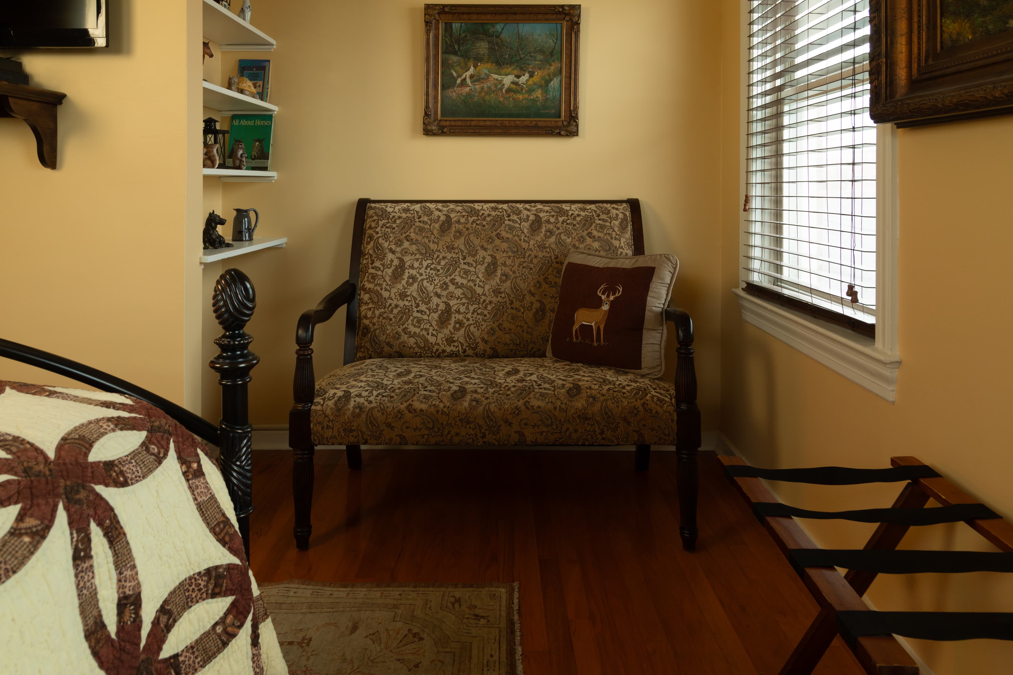 A decorated corner features a patterned loveseat with a deer-themed pillow, beside a window and shelves.