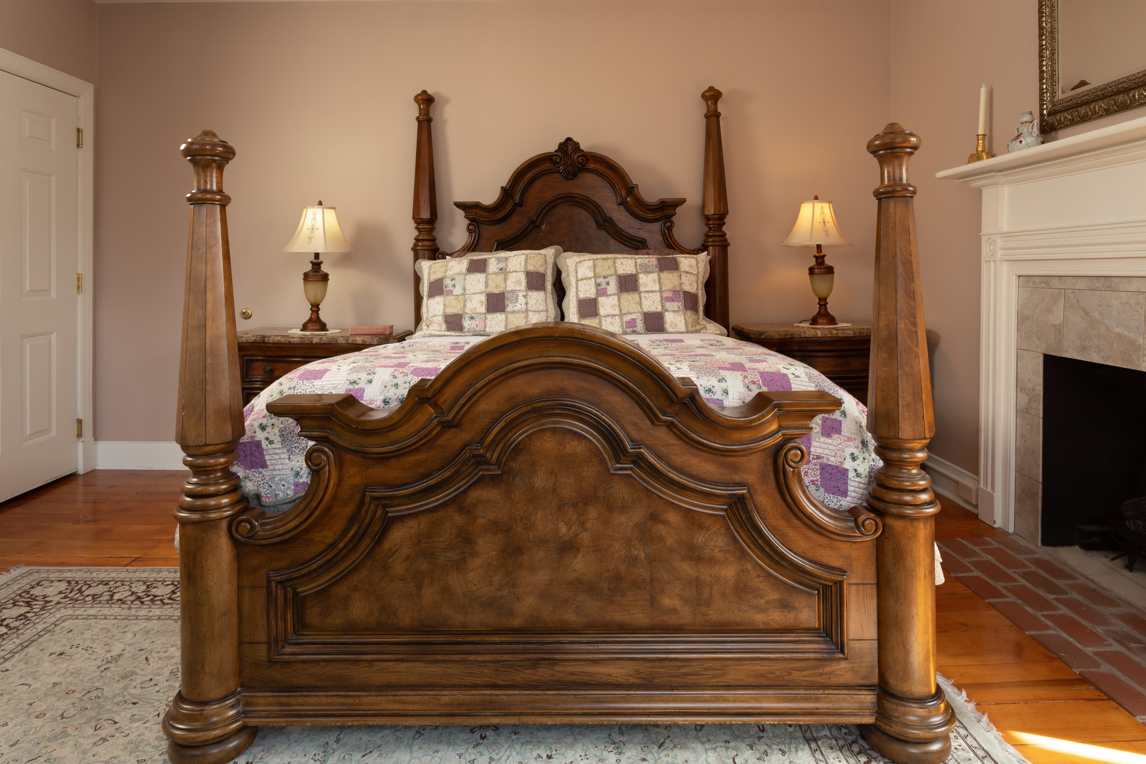 A wooden four-poster bed with a patterned quilt in a softly lit bedroom.