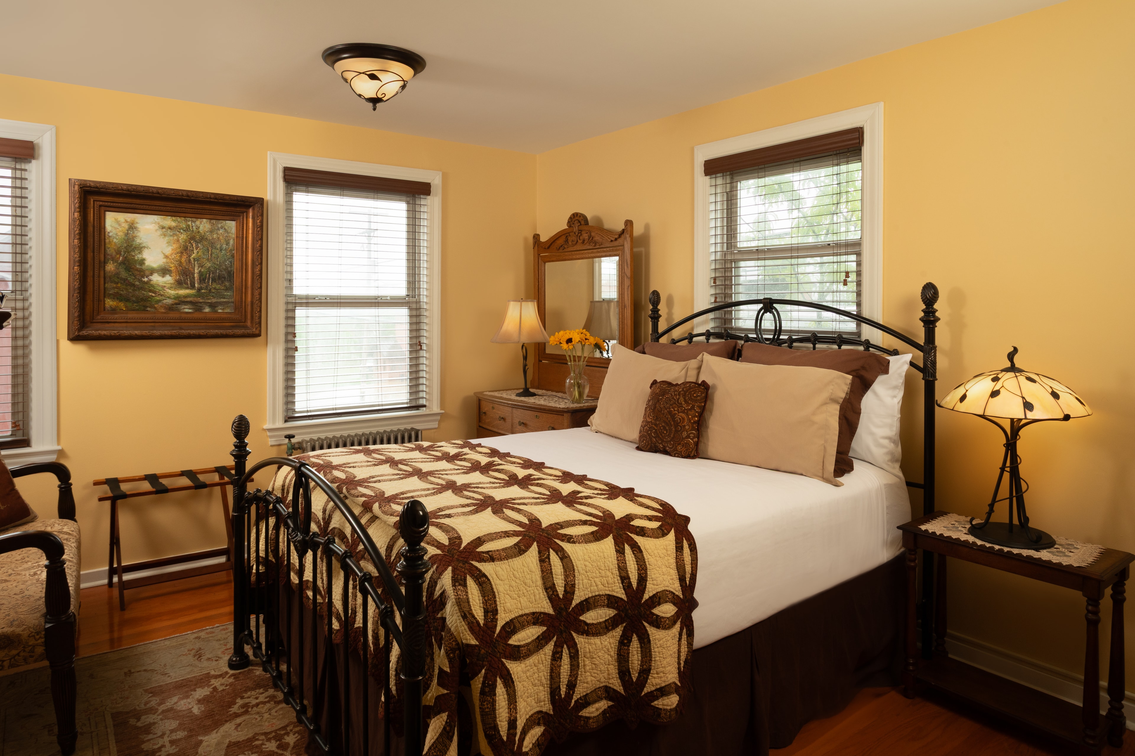 Cozy bedroom with a metal bed frame, yellow walls, and natural light from two windows.
