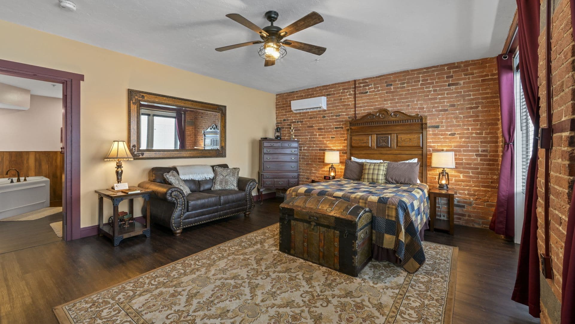 A cozy bedroom featuring exposed brick walls, a wooden bed, a couch, and warm lighting.