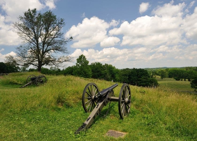 Civil War cannons overlooking the grassy fields and rolling landscape of Gettysburg Battlefield under a partly cloudy sky.